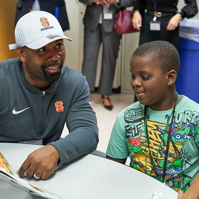 Syracuse Football Coach Fran Brown shares a book with children at a table during a United Way reading event.