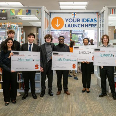 'Cuse Tank competition winners holding ceremonial checks in the Blackstone LaunchPad at Bird Library.