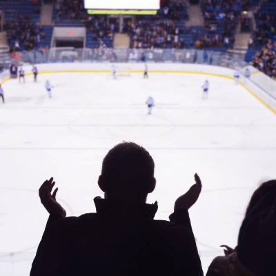 Spectator cheering at a live hockey game in a packed indoor arena with players on the ice