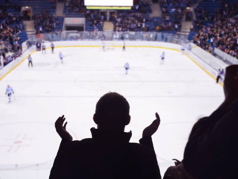 Spectator cheering at a live hockey game in a packed indoor arena with players on the ice