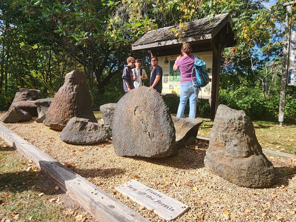 Students examining large fossil rock specimens displayed outdoors near an informational kiosk.