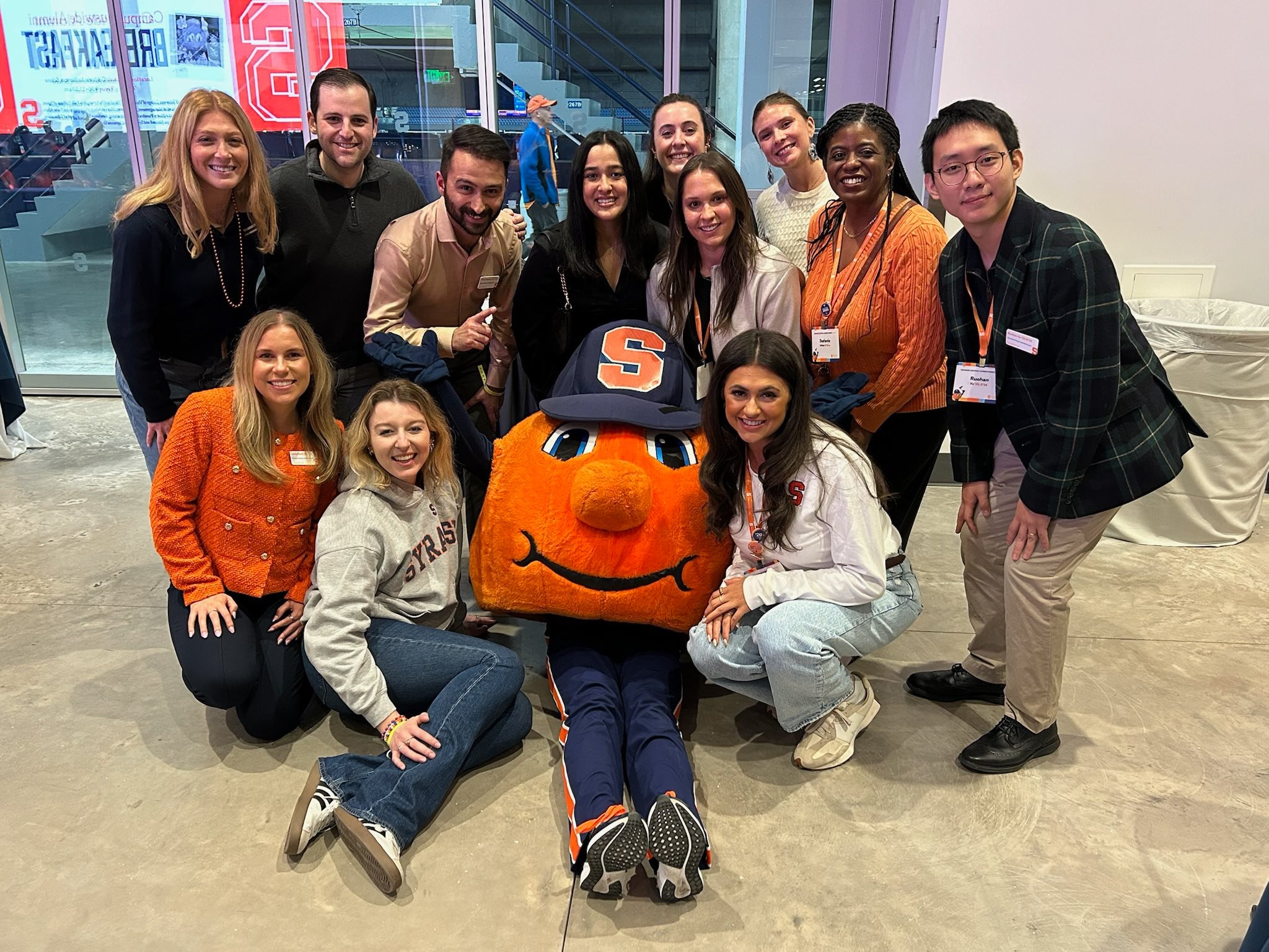 Large group of alumni and Otto mascot posing together in modern campus building atrium