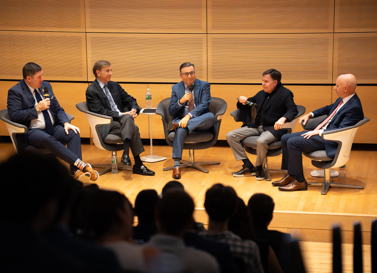 Five individuals seated on stage in modern chairs, engaged in a panel discussion.