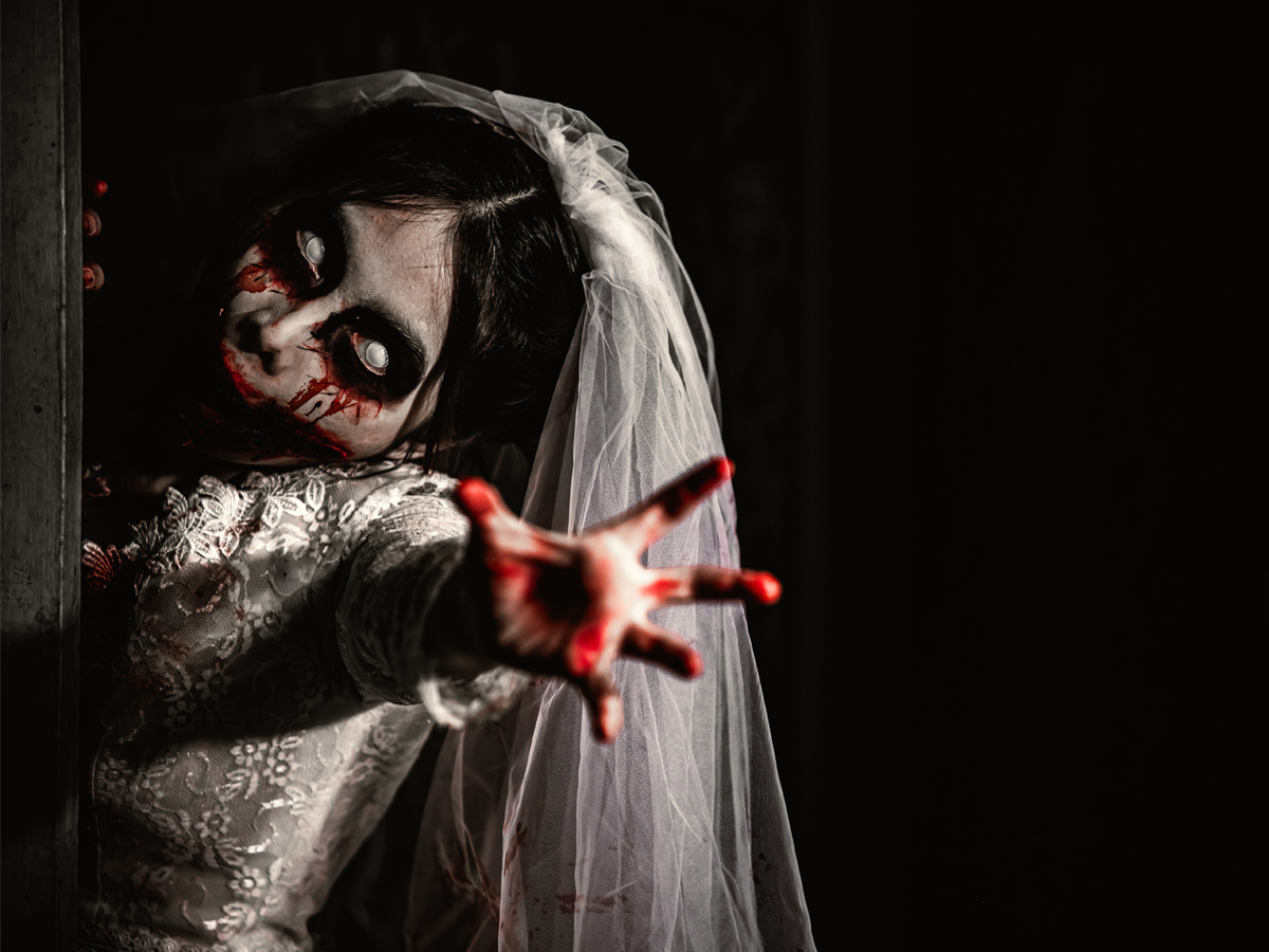 Bride in horror makeup with white contacts and blood effects reaching toward camera in dark setting.