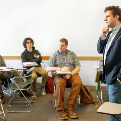 person speaking in front of a class with people seated at desks