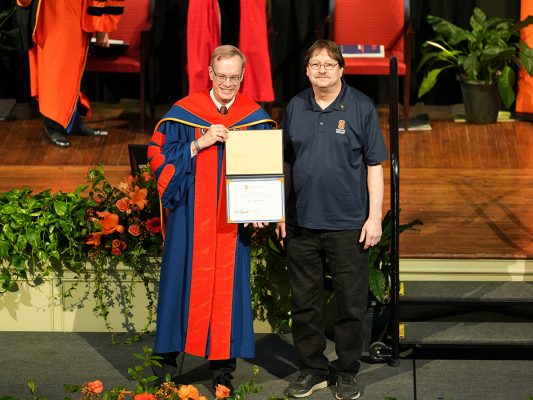 Chancellor Syverud (in academic regalia), presents a certificate the Jimmy Taylor Jr. at the One University Awards ceremony.