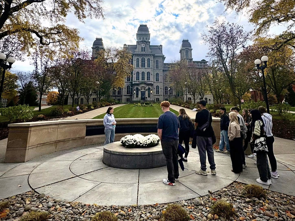 Group gathered around a circular flower bed in front of a large stone building with towers