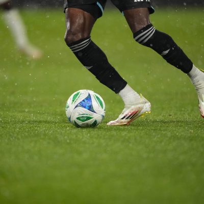 Soccer players competing for ball on wet field, close-up of legs and cleats in motion