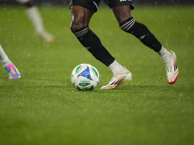 Soccer players competing for ball on wet field, close-up of legs and cleats in motion