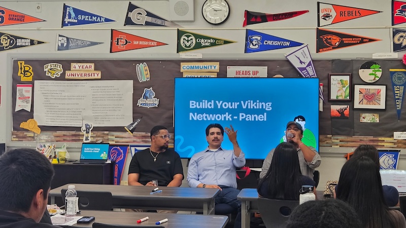 Three speakers seated for a “Build Your Viking Network” panel in a classroom with university pennants and educational posters.
