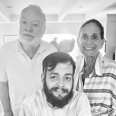Man and woman standing with their grandson sitting in front of them.