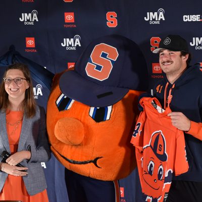 Otto the Orange pictured with woman and man, man holding a Otto jersey