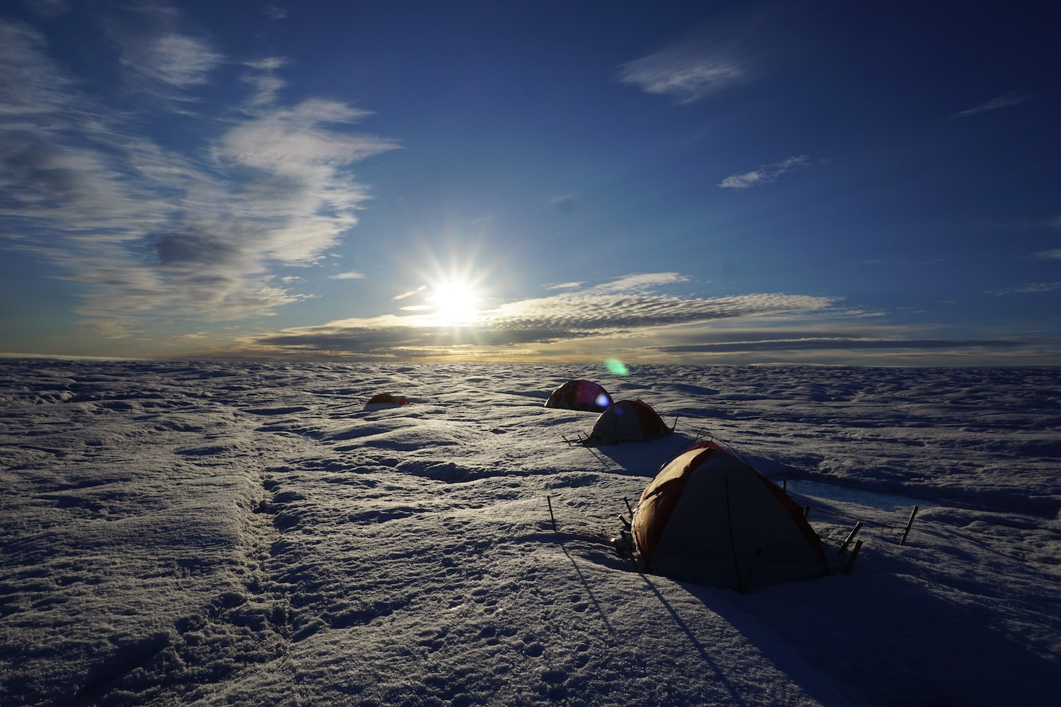 Field camp tents on snowy Greenland landscape at sunrise.