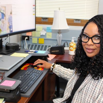 A person seated at an office desk working on a computer with a large curved monitor