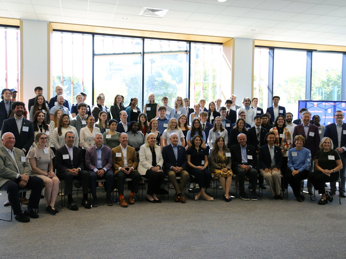 A large formal group photo of Lee Scholars students and program supporters gathered in a bright conference room with floor-to-ceiling windows, arranged in seated and standing rows.