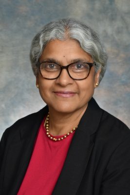 Portrait of a person wearing a red top, a black blazer and a gold beaded necklace.