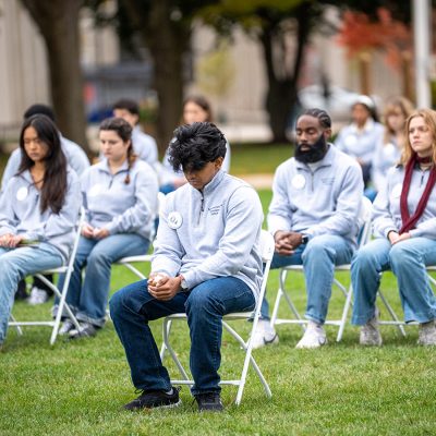 Remembrance Scholars in grey sweatshirts sit in chairs on the Quad