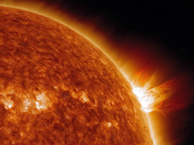 Close-up of the sun's surface with a solar flare erupting, showcasing intense heat and energy against the dark backdrop of space.