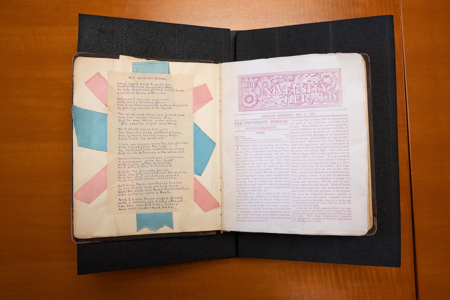 Open scrapbook showing a poem with blue and pink paper strips on the left page and newspaper article on the right.