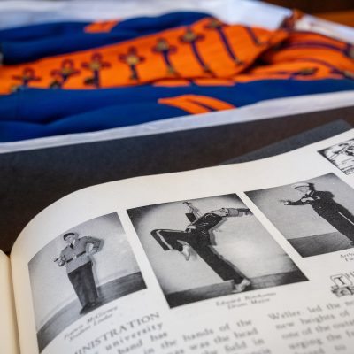 A black and white yearbook page displayed in front of a blue and orange marching band uniform.