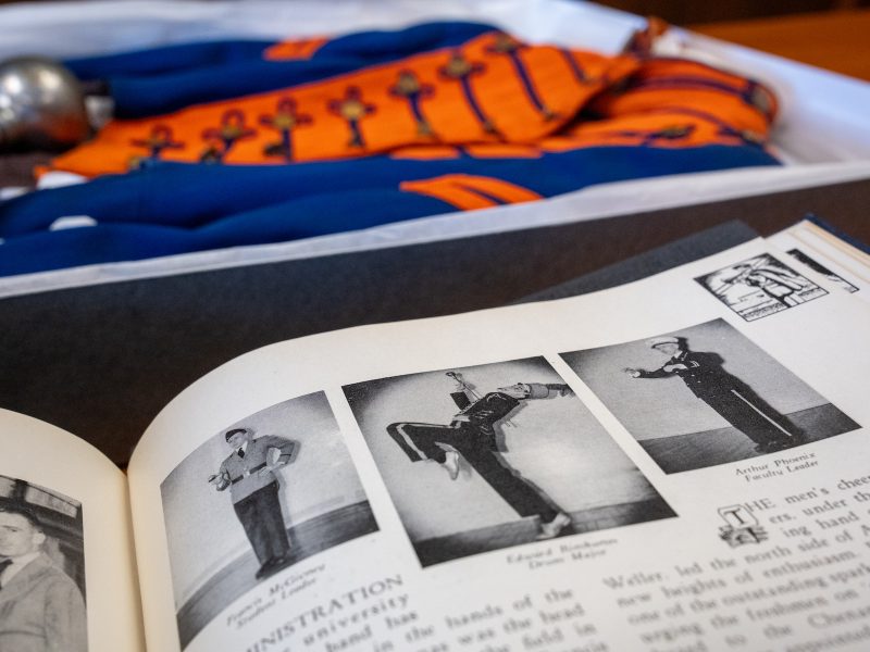 A black and white yearbook page displayed in front of a blue and orange marching band uniform.