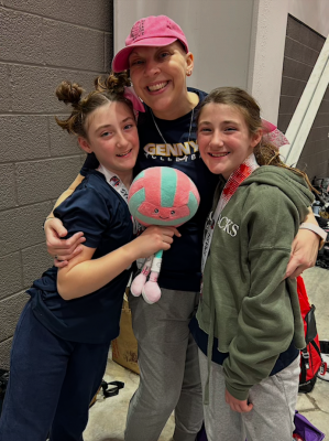 Three people with medals pose indoors; one holds a plush volleyball toy.