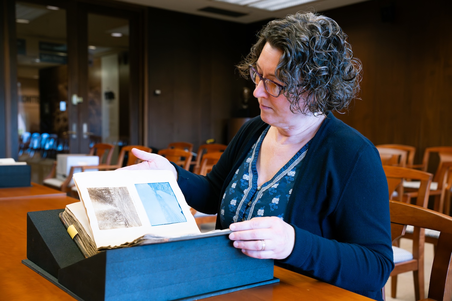 Person examining a book with photographs in a library.