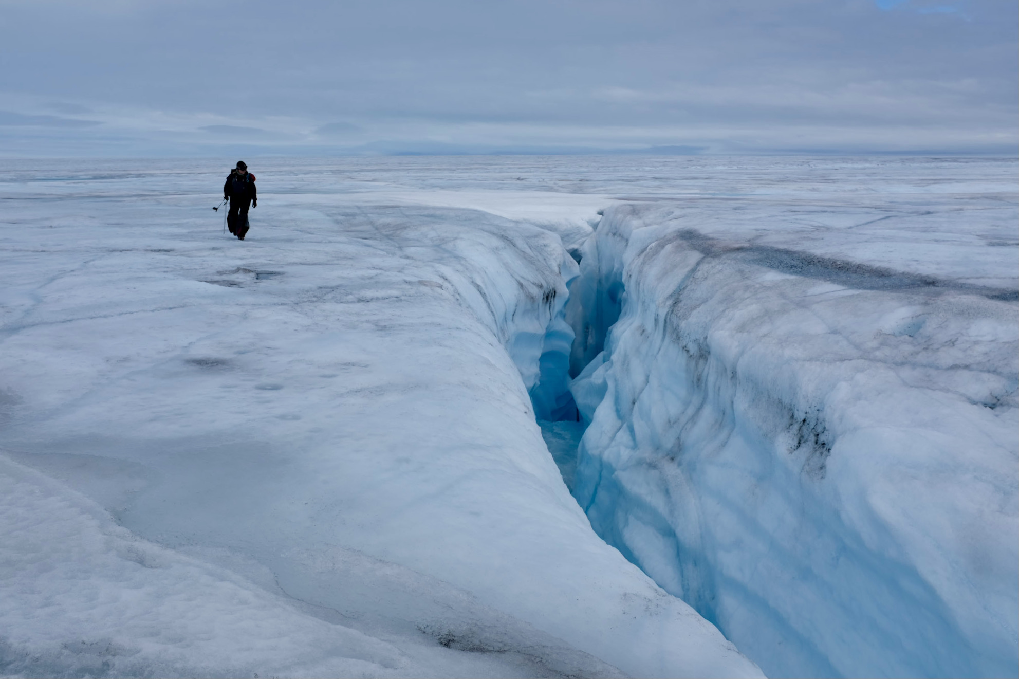 Researcher walking near crevasse in glacier. 