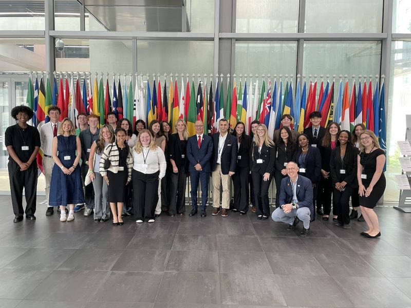 Group of professionals posing in front of international flags inside a modern building.
