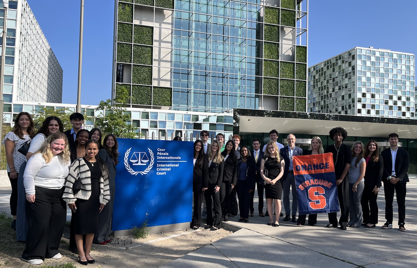 Group outside International Criminal Court holding 'Orange Syracuse' banner.