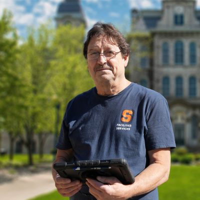 Person in a Syracuse shirt holding an Ipad in front of the Hall of Languages