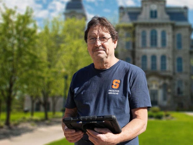 Person in a Syracuse shirt holding an Ipad in front of the Hall of Languages