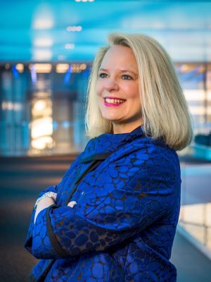 Person wearing a blue patterned jacket, standing with arms crossed.