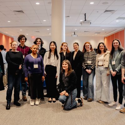 A group of people standing and kneeling in a conference room with tables covered in orange cloth.