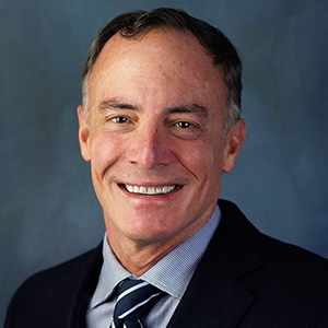 Man with dark hair, smiling, wearing a jacket and tie