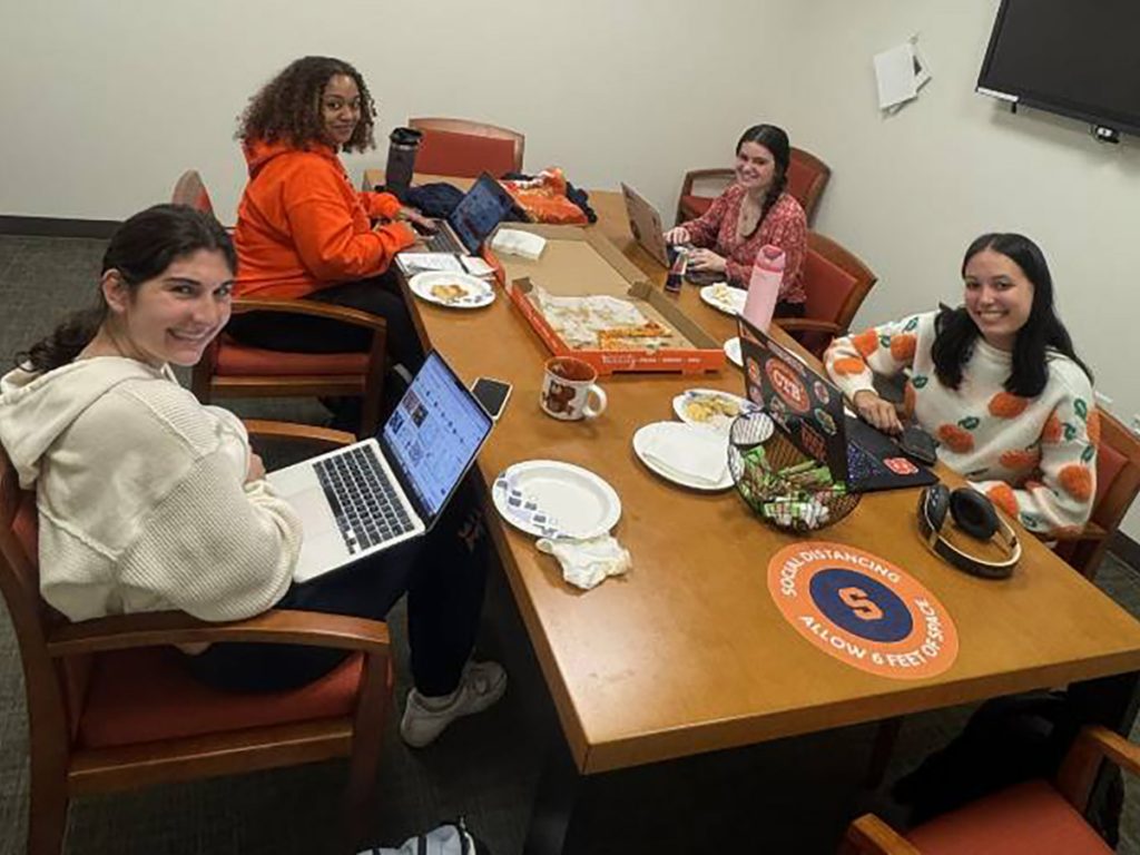 Four women students it around a table with laptops working on a project.