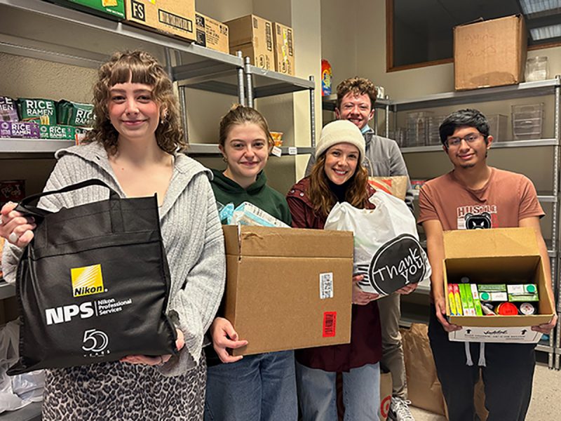 Students hold boxes and bags of food in the Coach Mac Food Pantry at Hendricks Chapel