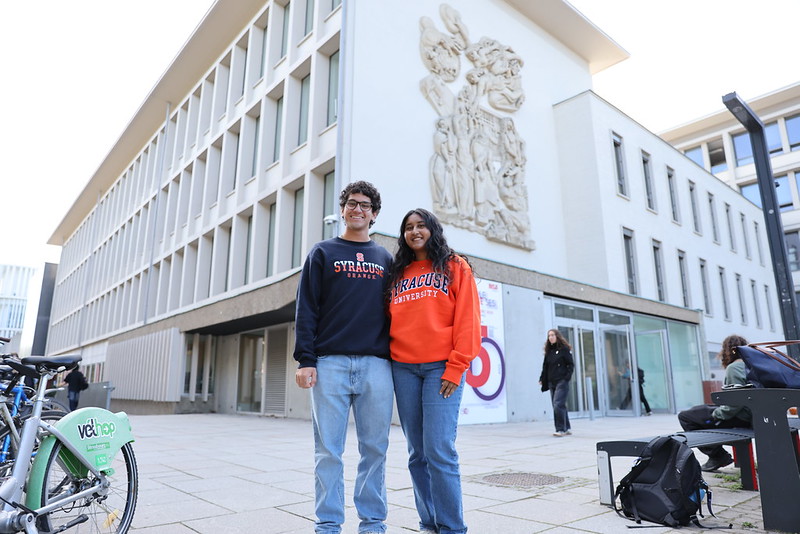 "Syracuse students in front of white building with decorative relief sculpture.