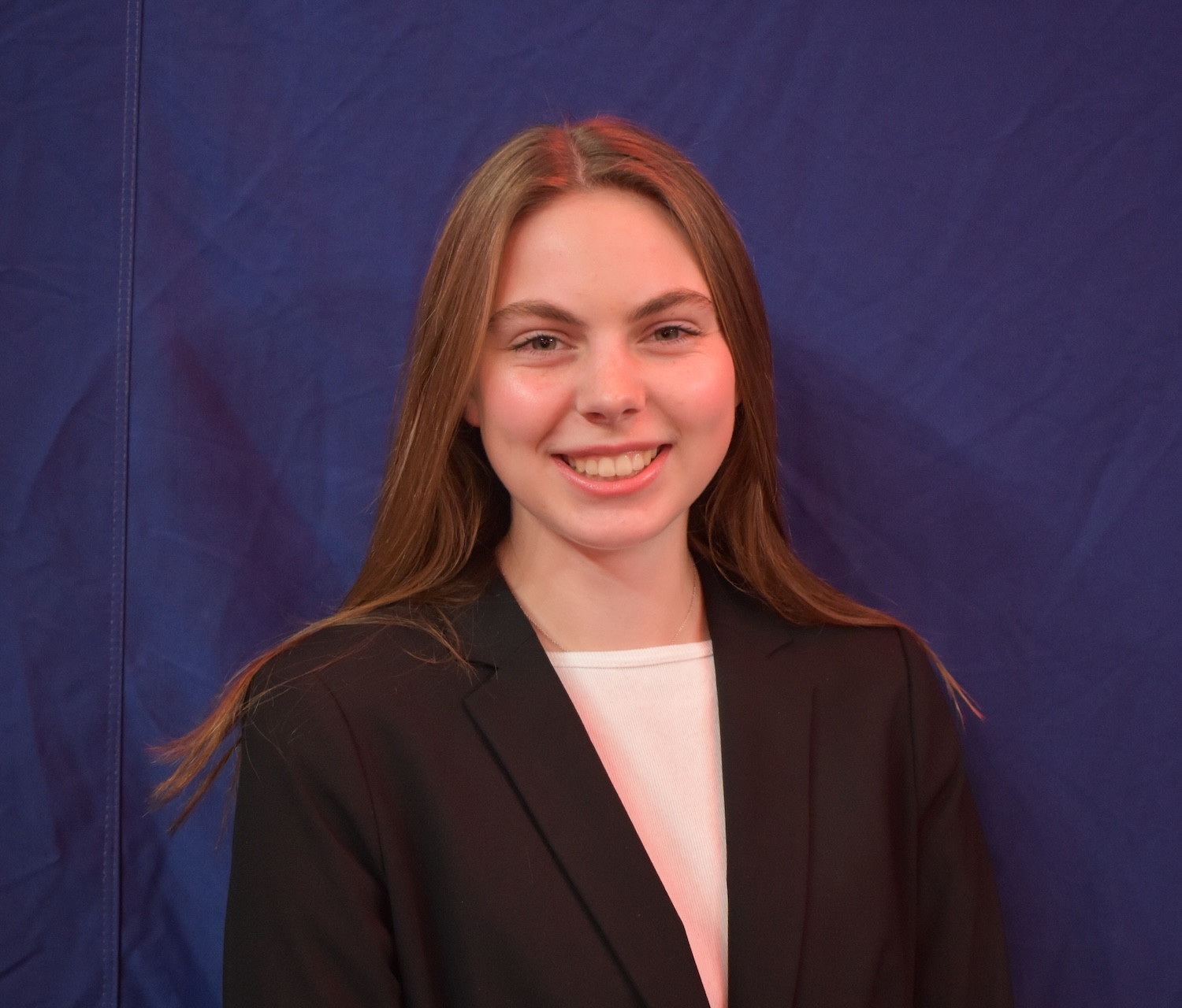 Person wearing a black blazer over a light-colored top, standing against a solid blue background.