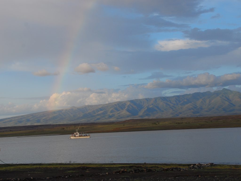 A research vessel on calm waters with mountain ranges visible in the distance under cloudy skies.