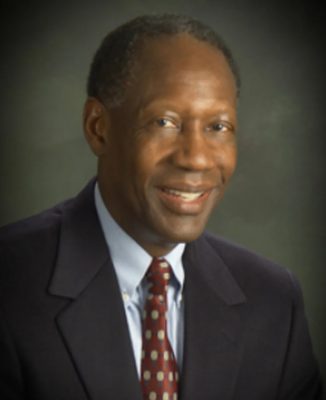 A person smiles while posing for a headshot in front of a dark backdrop.