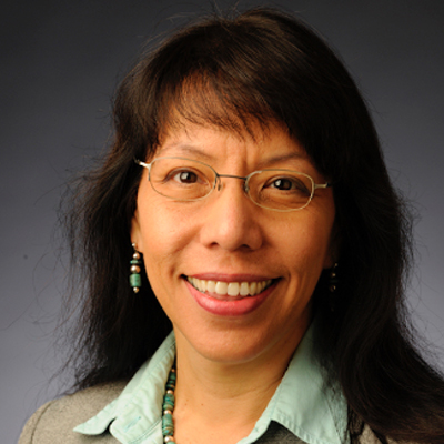 A person smiles while posing for a headshot in front of a grey backdrop.