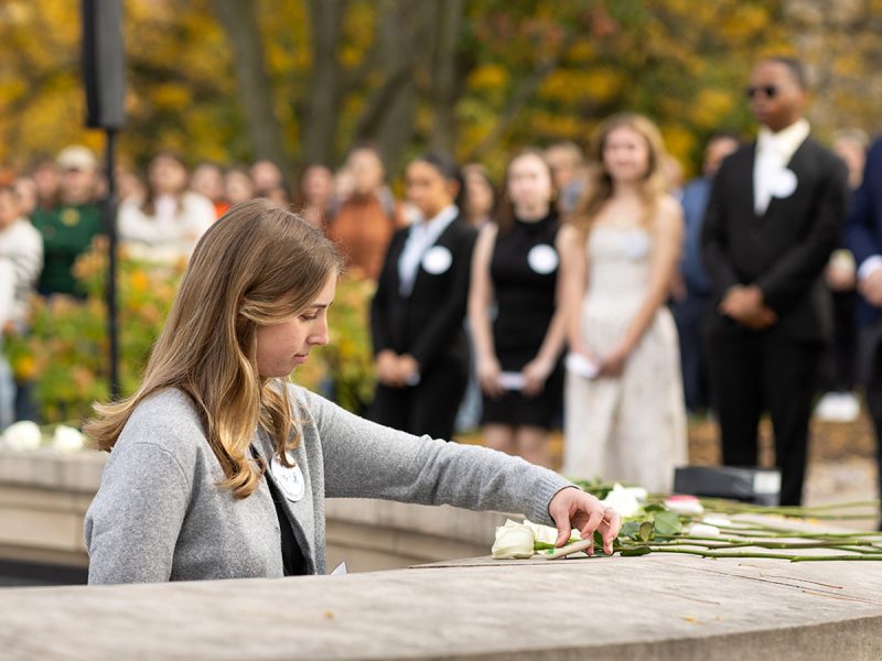 A Remembrance Scholar lays a white rose on the Wall of Remembrance