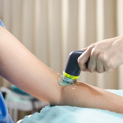 An ultrasound is performed on the left arm of a patient in a medical gown.