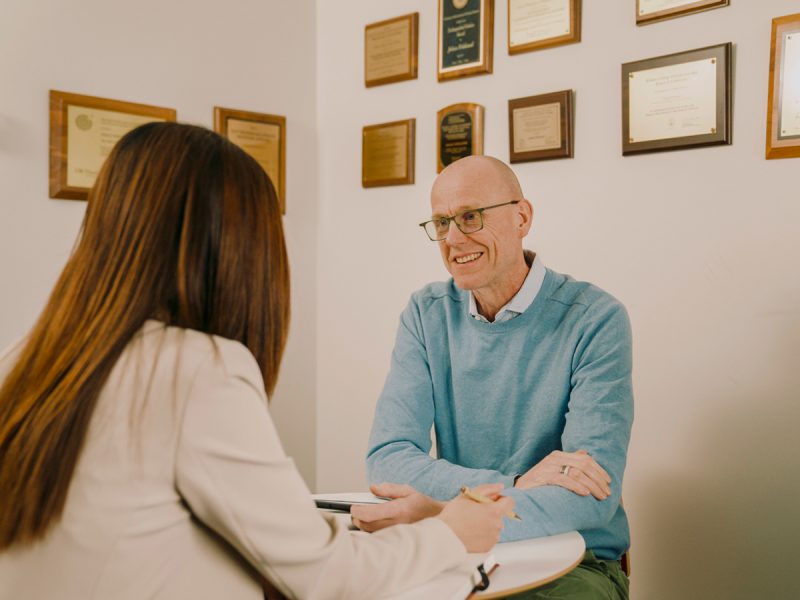 Professional meeting between two people in an office with framed certificates and awards on the wall.