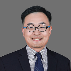 Dark-haired man, smiling and wearing glasses, in a jacket and tie.