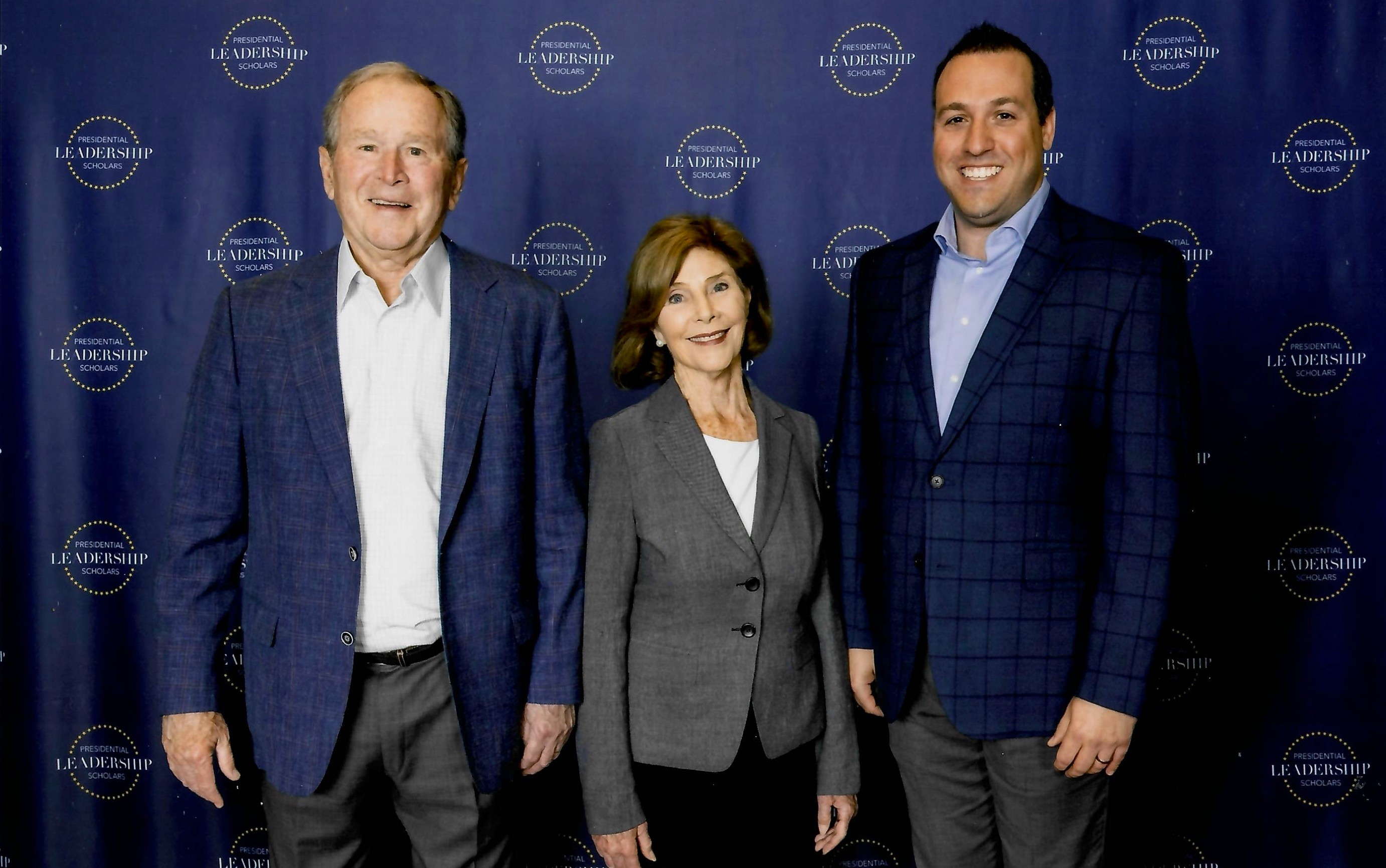 Three people standing in front of a dark blue backdrop with repeated “Leadership” logos.