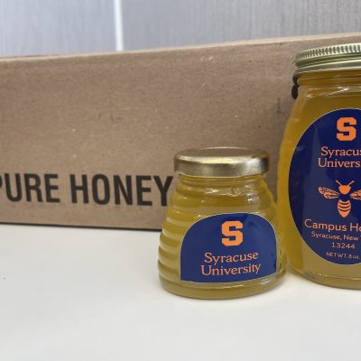 Two jars of honey labeled “Syracuse University” and “Campus Honey” sit in front of a box marked “Pure Honey.”