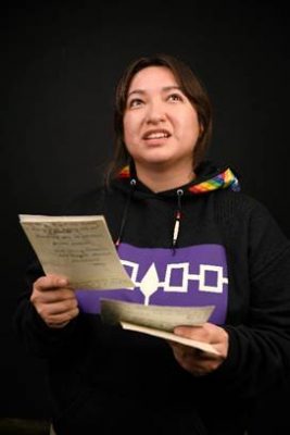 Woman with Indigenous shirt on reading from a script