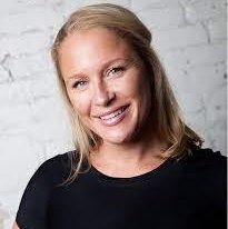A person smiles for a headshot while standing in front of a white wall.